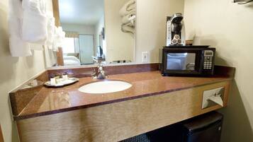 A bathroom with a sink, a mirror, a towel rack, a coffee maker, and a trash bin.