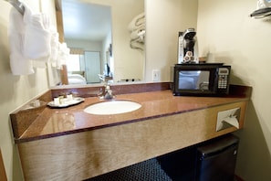 A bathroom with a sink, a mirror, a towel rack, a coffee maker, and a trash bin.