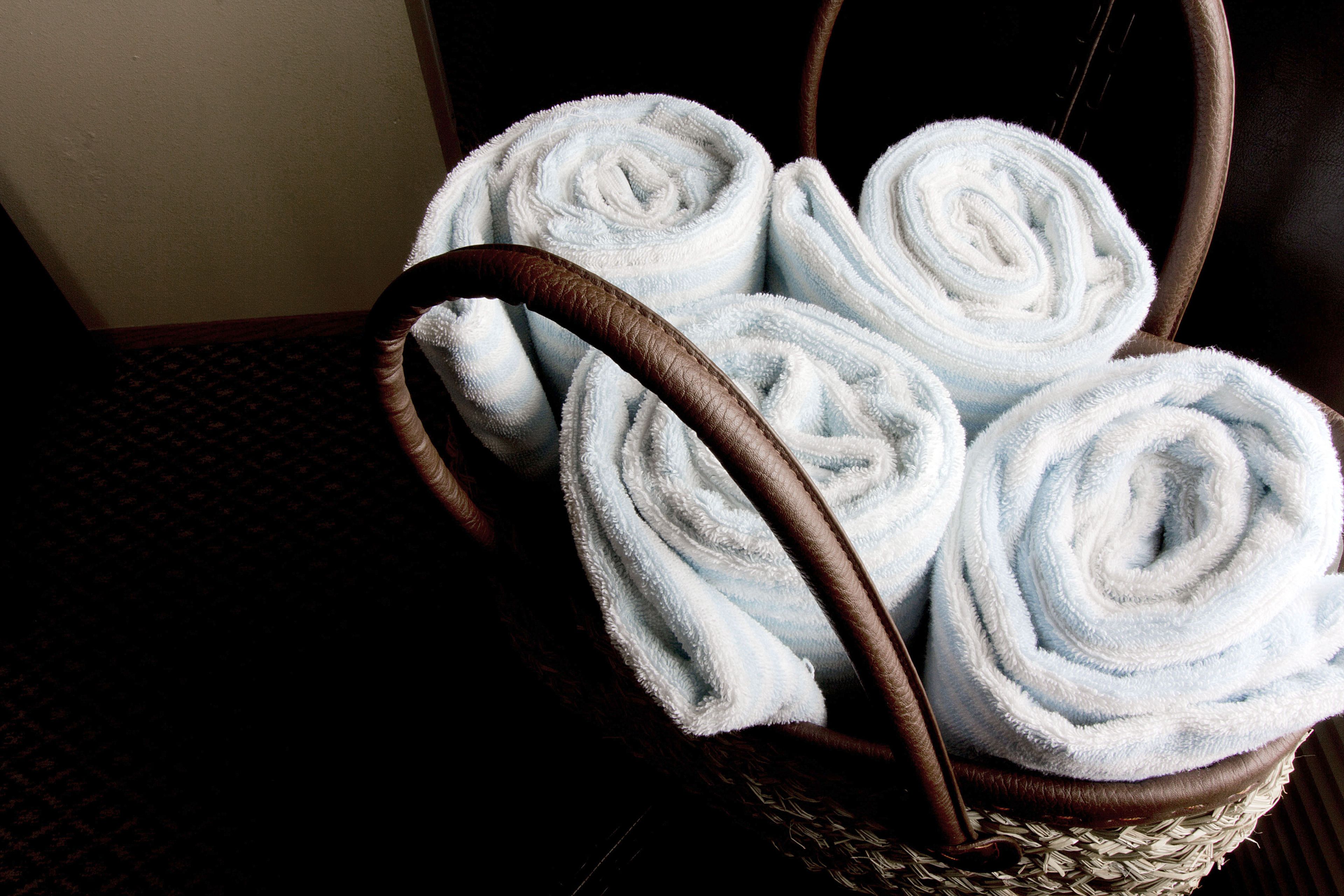 A wicker basket containing four neatly rolled white towels.
