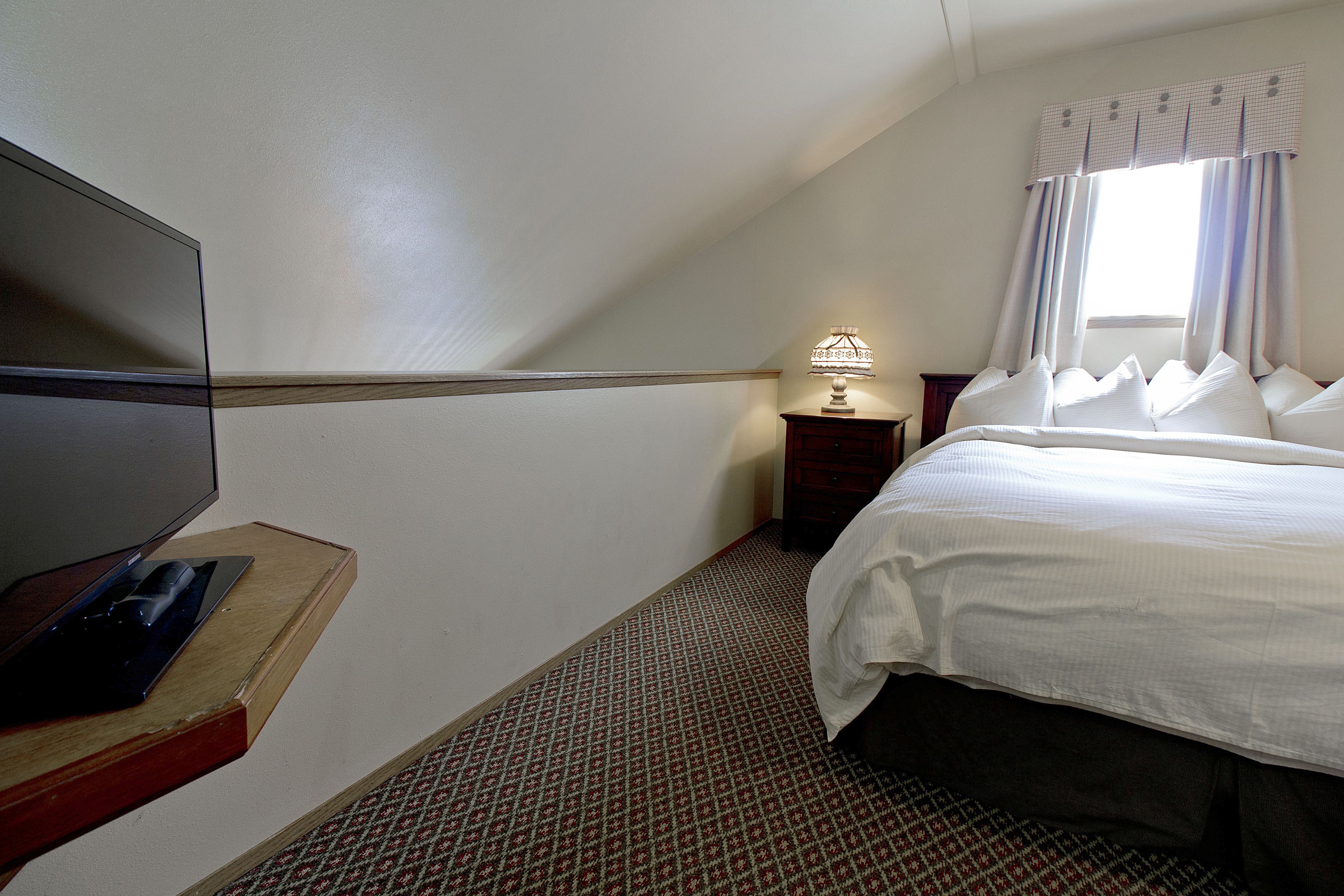 Una habitación de hotel con una cama, un escritorio con lámpara, un televisor y una alfombra estampada.