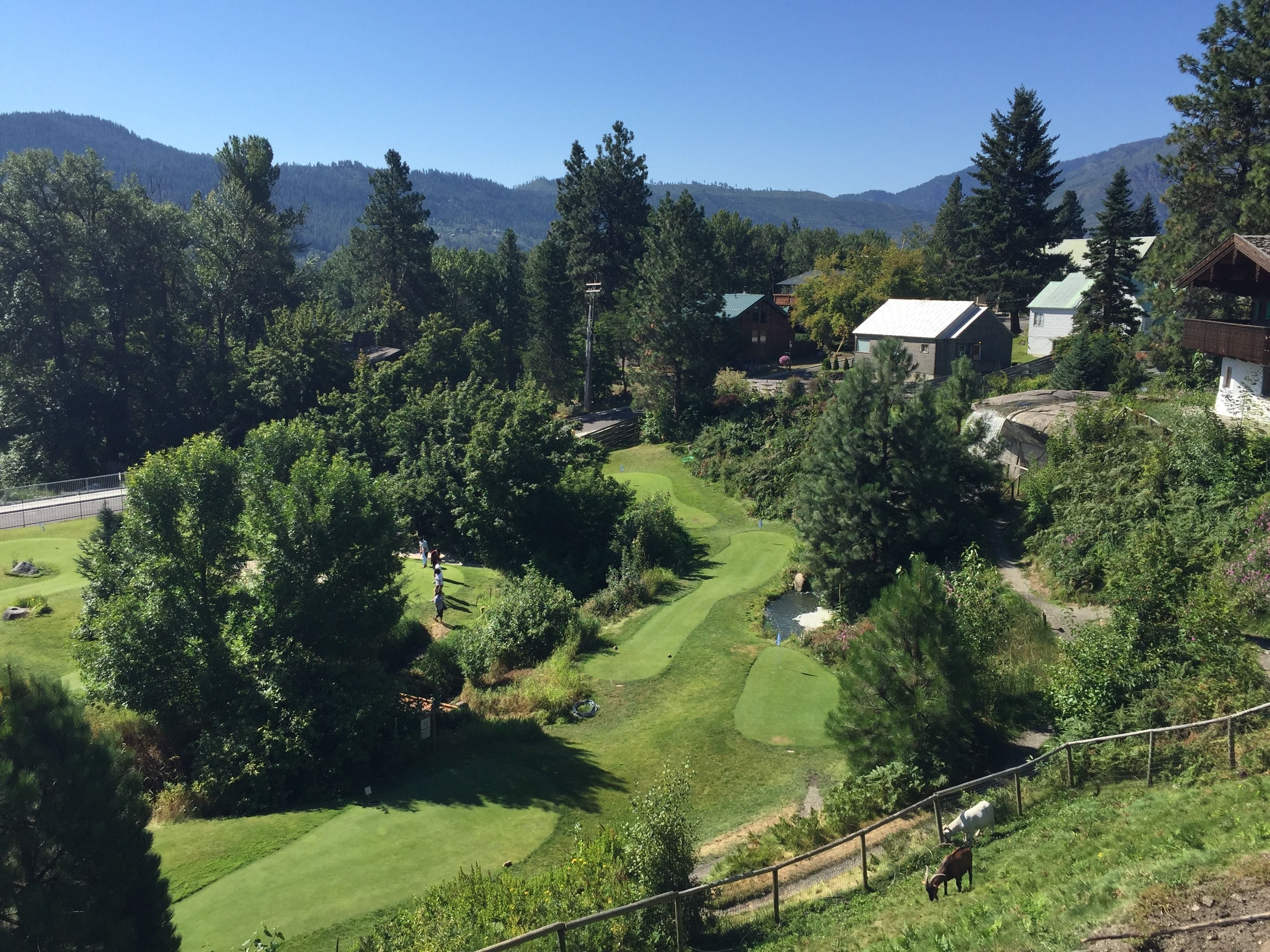 Ein Golfplatz mit Klubhaus, umgeben von Bäumen und Hügeln.
