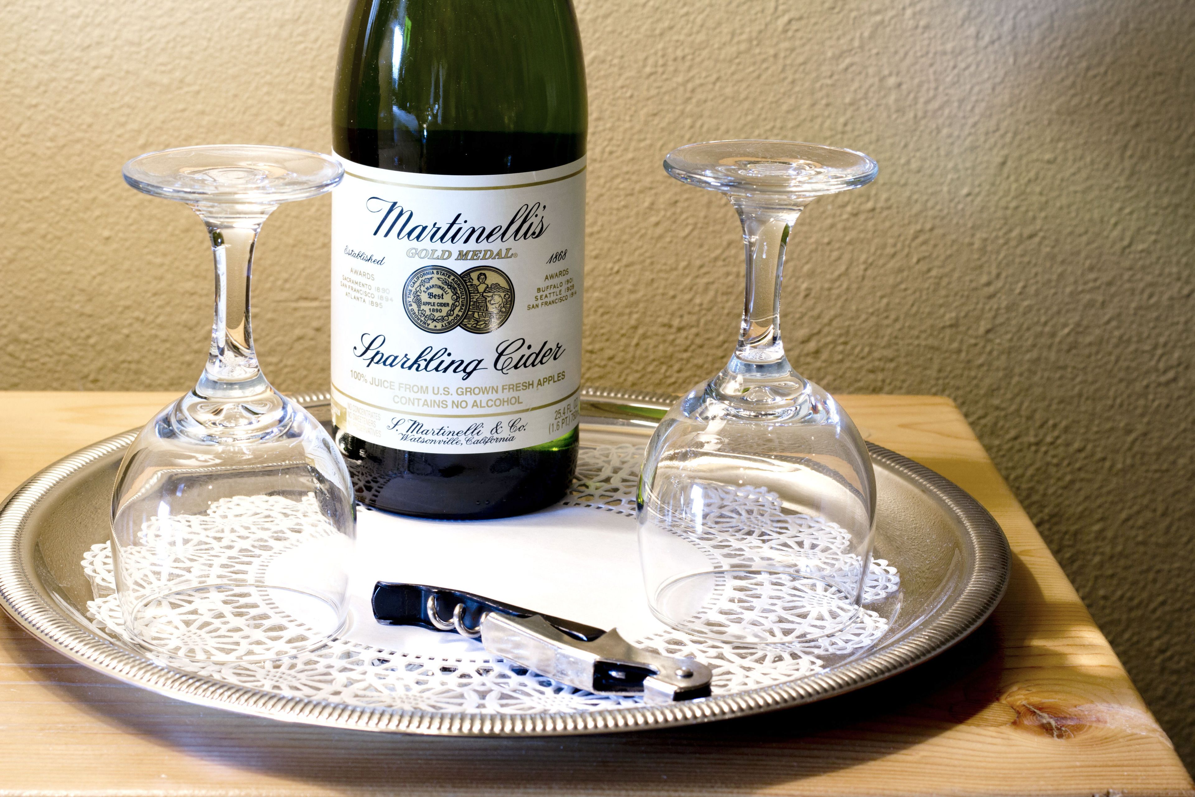 Ein Btl. Martinelli's Sprudelzider auf einem Tablett mit zwei Weingläsern.
