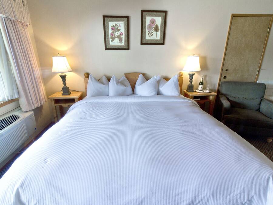 A hotel room with a large bed, two bedside lamps, a chair, and two framed floral pictures on the wall.