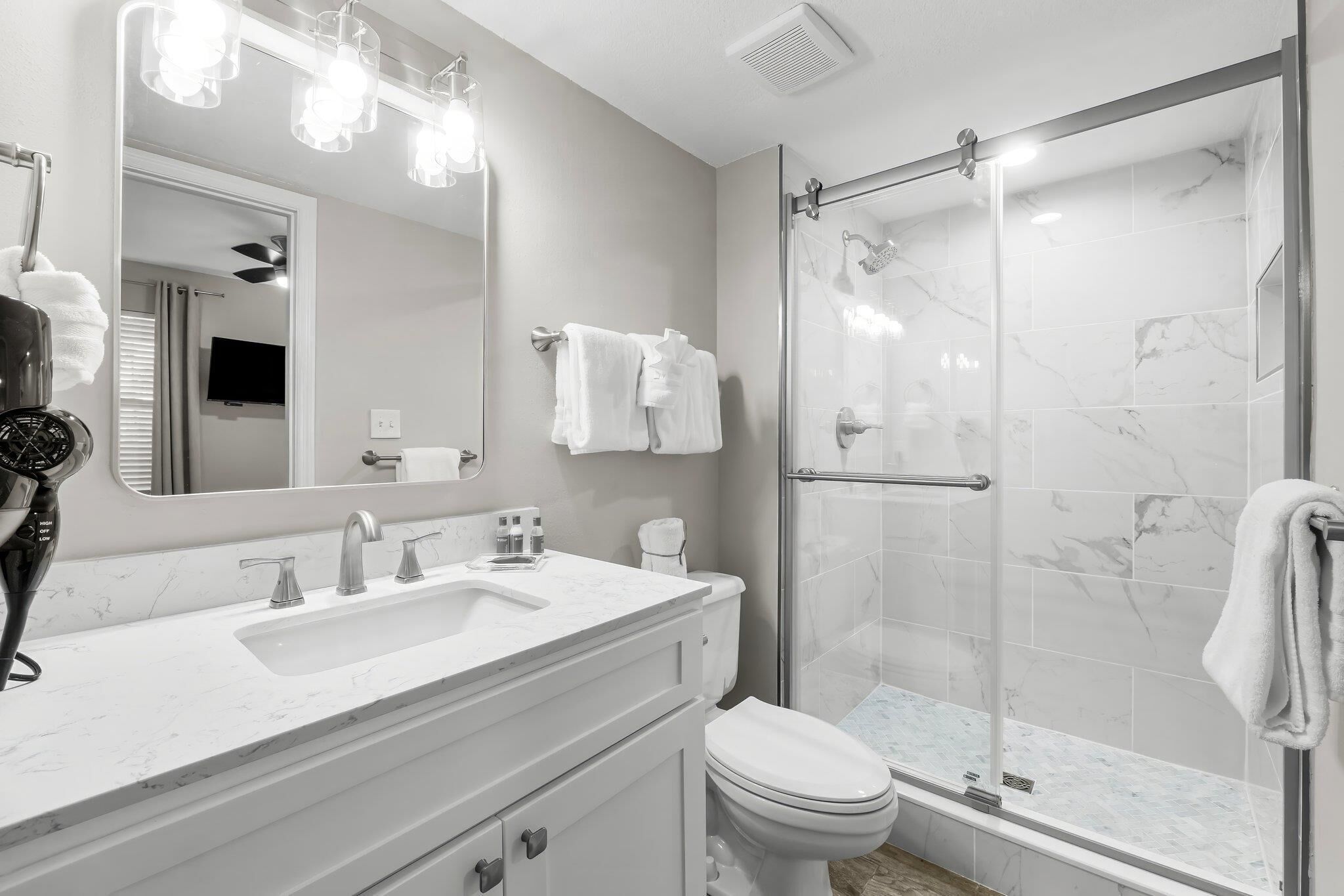 A modern bathroom with a white vanity, a large mirror, a shower with a glass door, and a toilet.