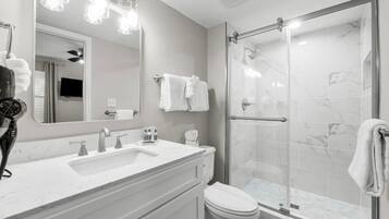 A modern bathroom with a white vanity, a large mirror, a shower with a glass door, and a toilet.