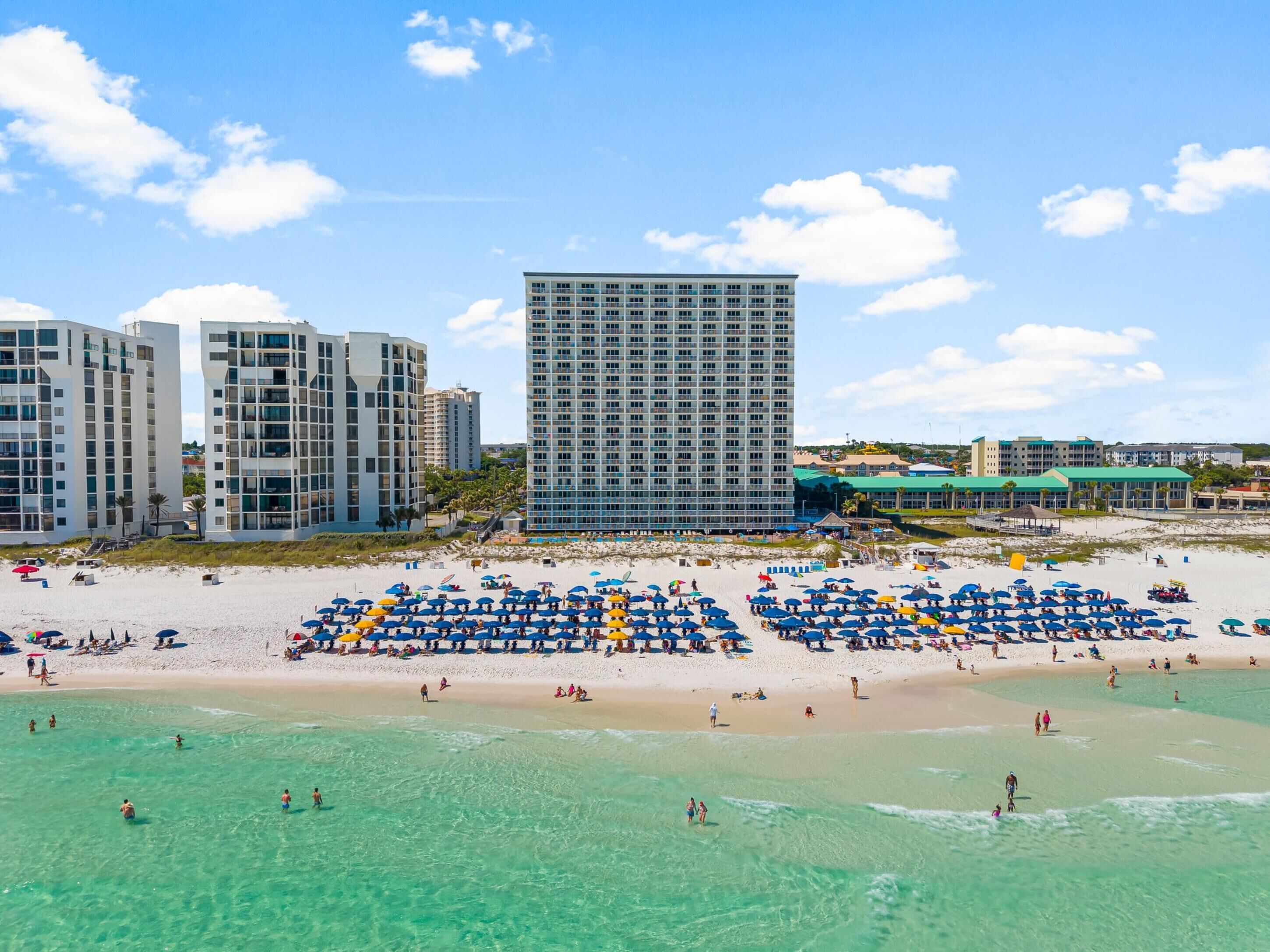 A beachside hotel with multiple high-rise buildings, a sandy beach with umbrellas, and clear turquoise waters.