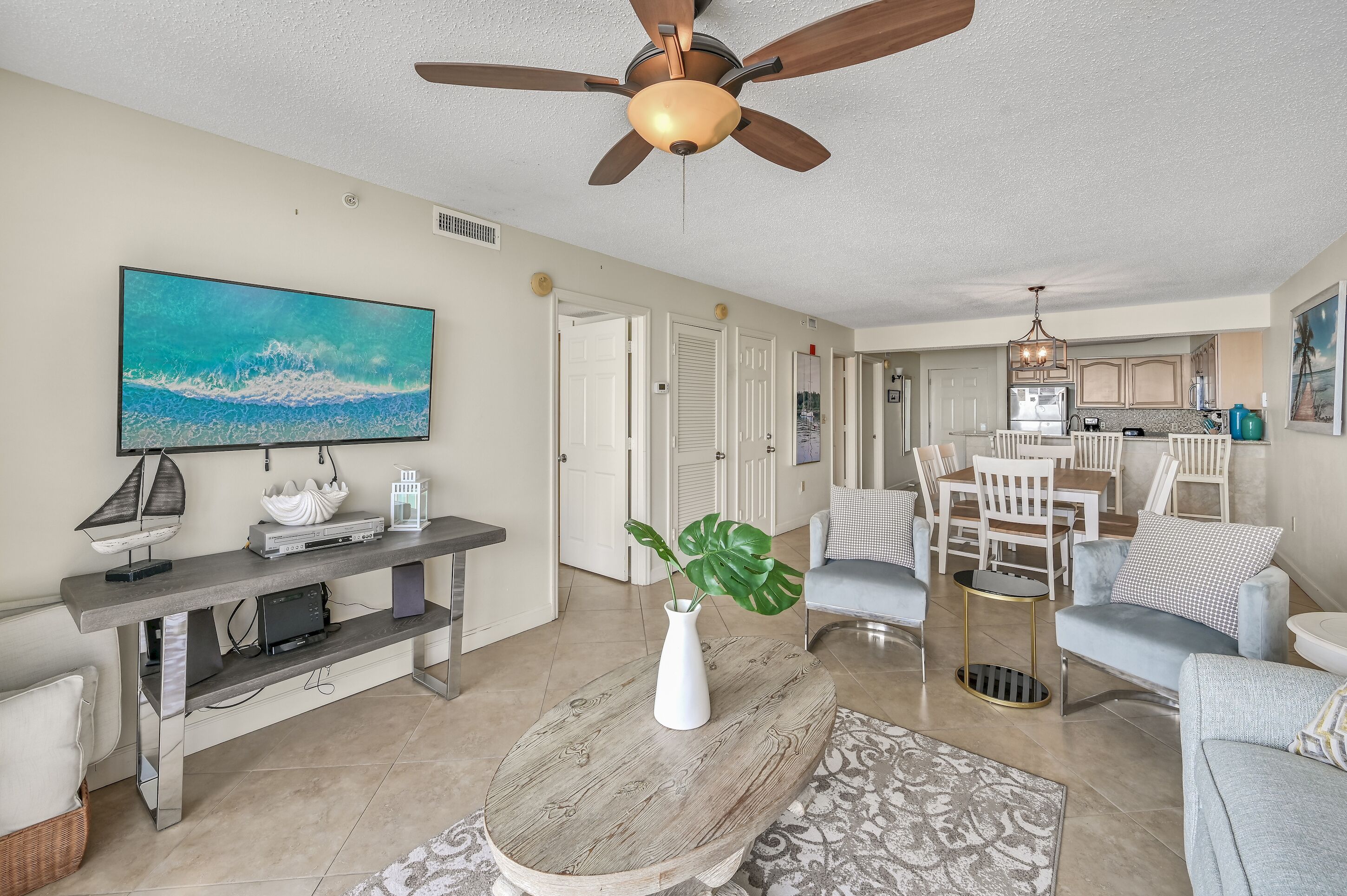 A living room with a ceiling fan, a flat-screen TV, a coffee table, and a dining area with chairs and a table.