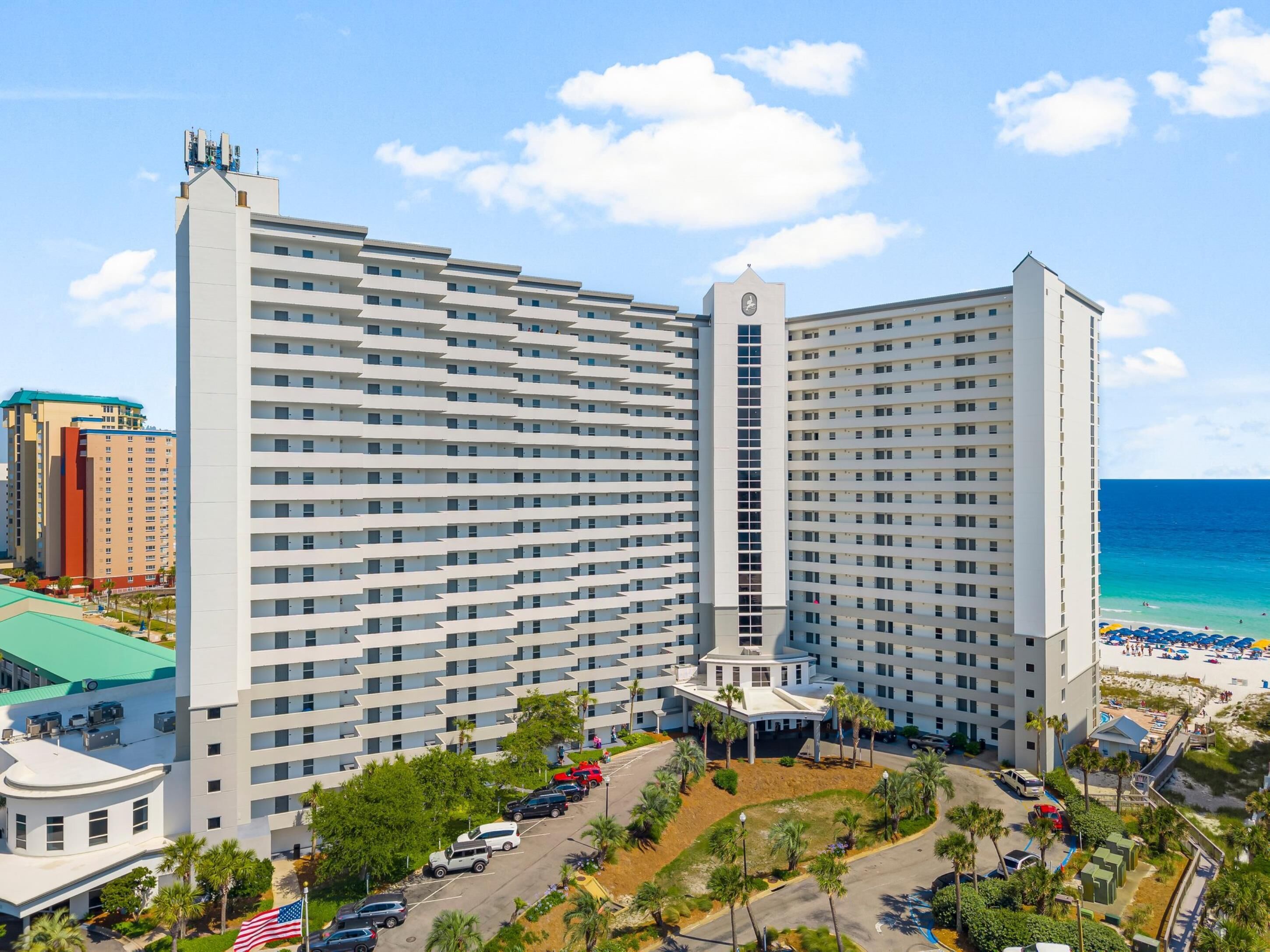 Un hotel di grattacielo con numerosi piani, una torre dell'orologio centrale e vista sulla spiaggia.