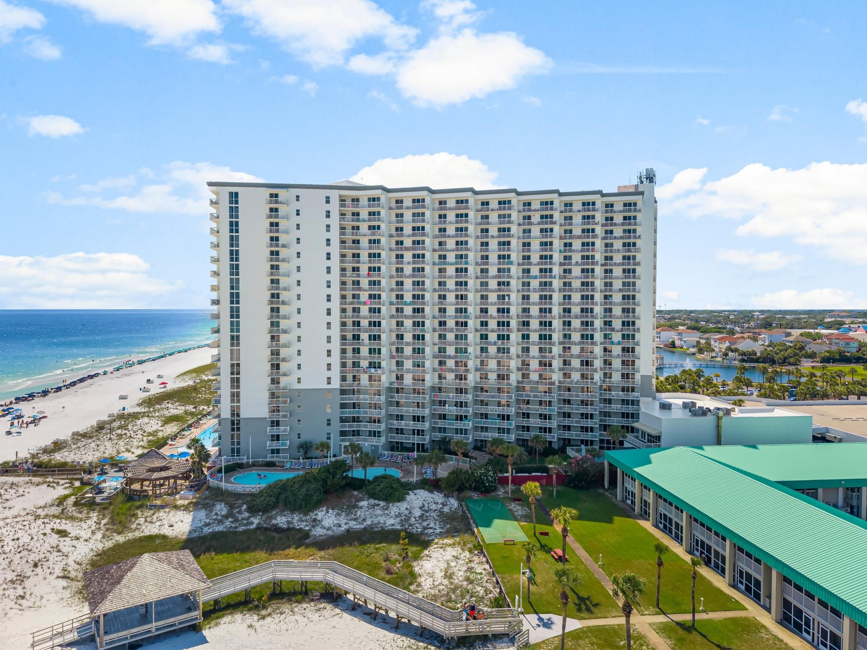 A high-rise hotel with multiple balconies, a beach view, and a pool area.