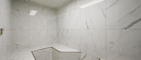A modern bathroom with white marble tiles, a skylight, and a shower area.