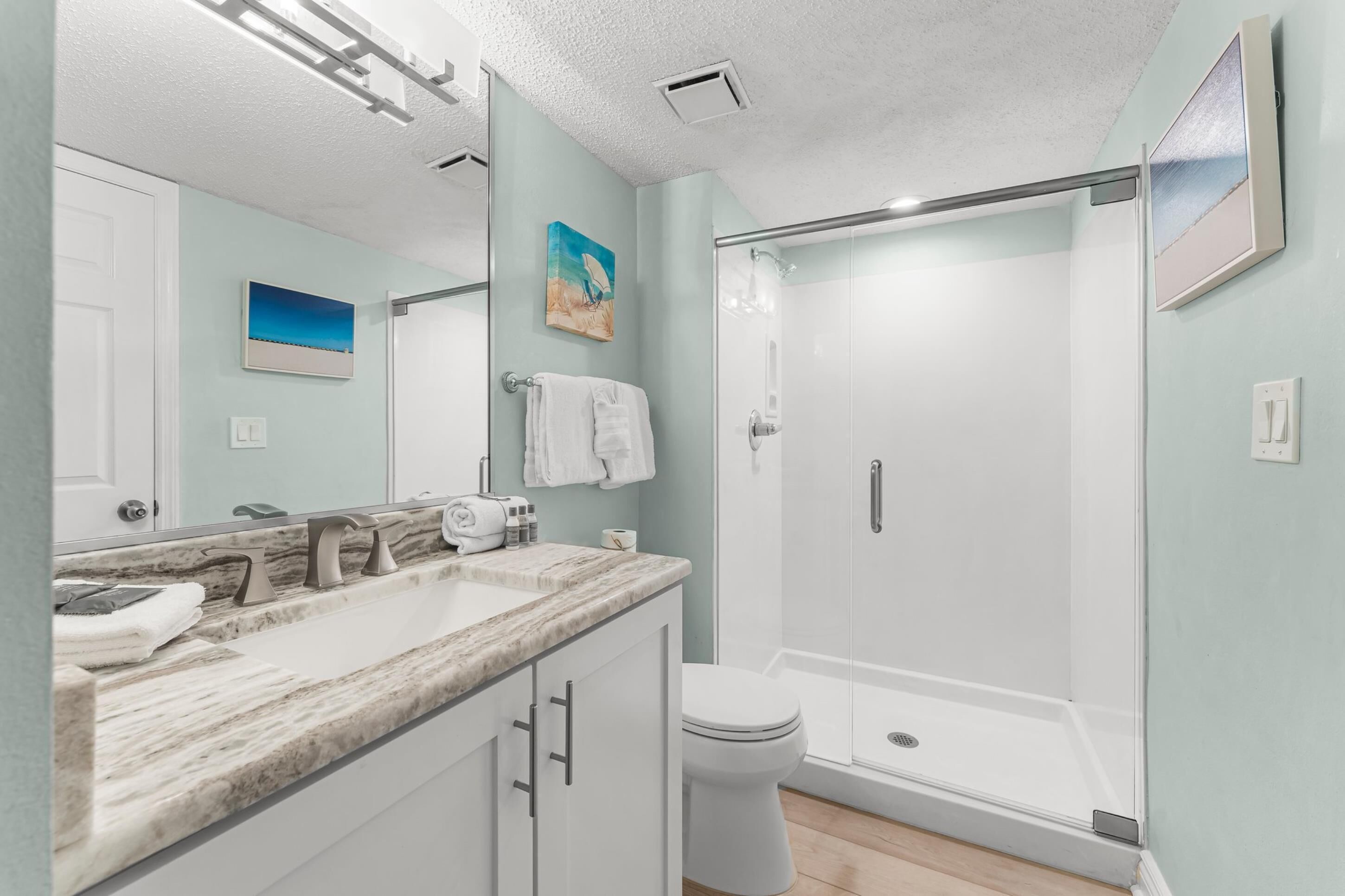 A modern bathroom with a marble countertop, a glass shower enclosure, and a toilet.