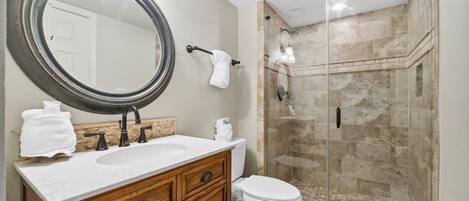 A bathroom with a wooden vanity, a large mirror, a toilet, and a glass-enclosed shower.