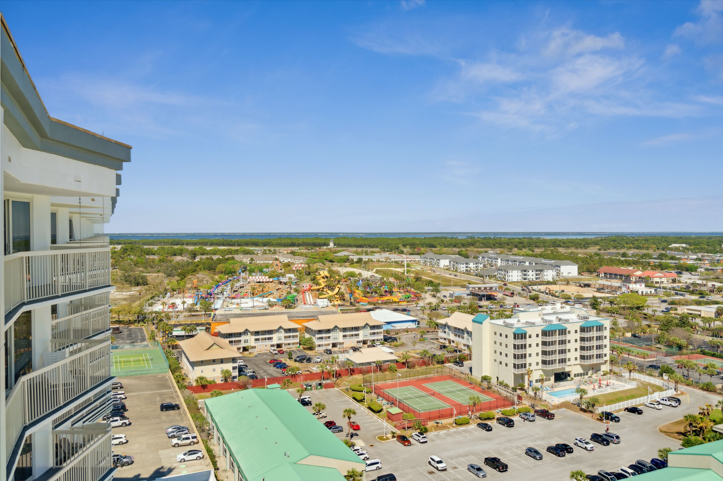 A high-rise hotel with multiple floors, a parking lot, and a sports complex with tennis courts and a playground.