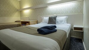 Habitación de hotel con dos camas, una mesita de noche y una repisa en la pared.