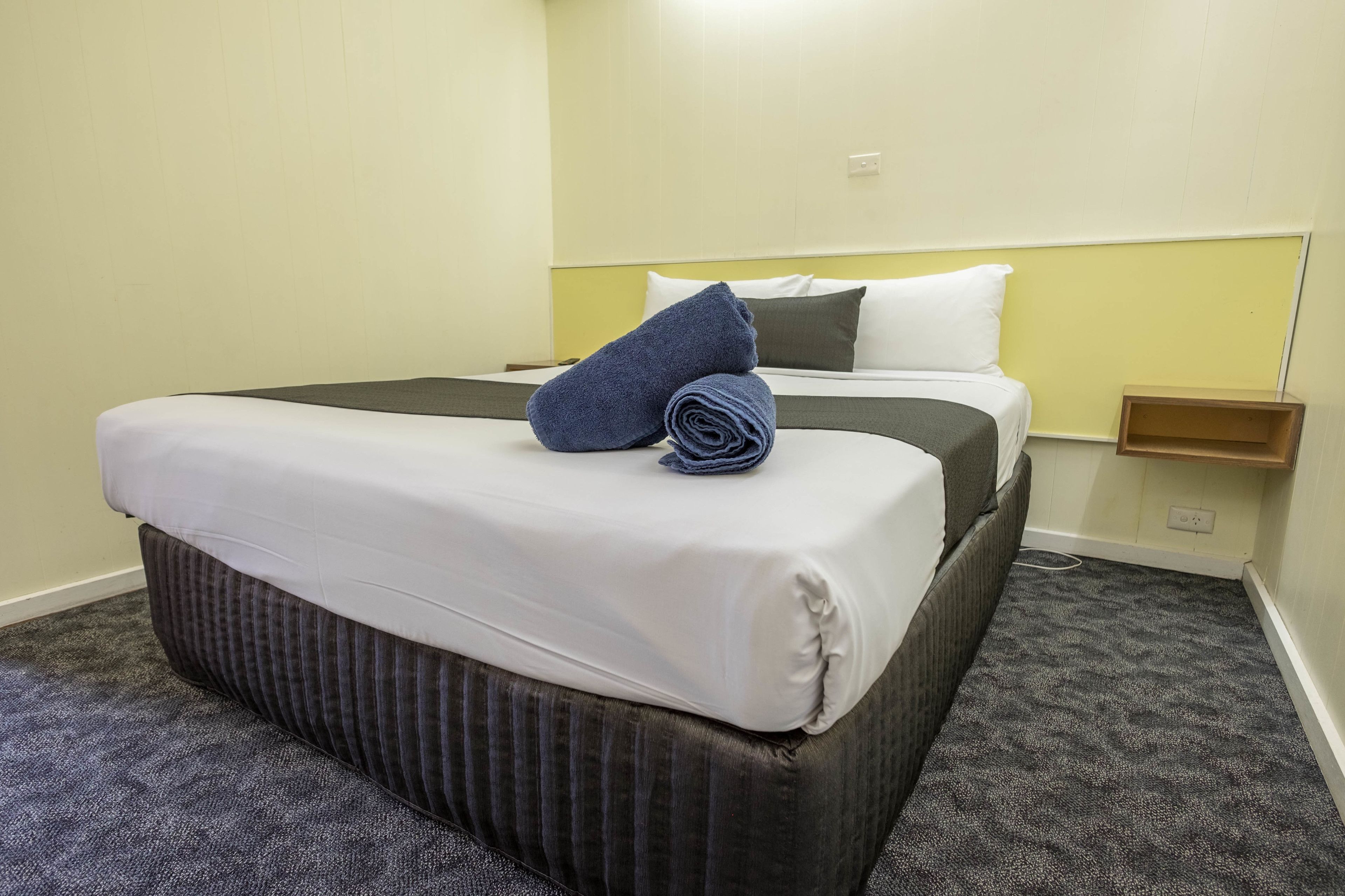 Una habitación de hotel con una cama, una mesita de noche y un enchufe.