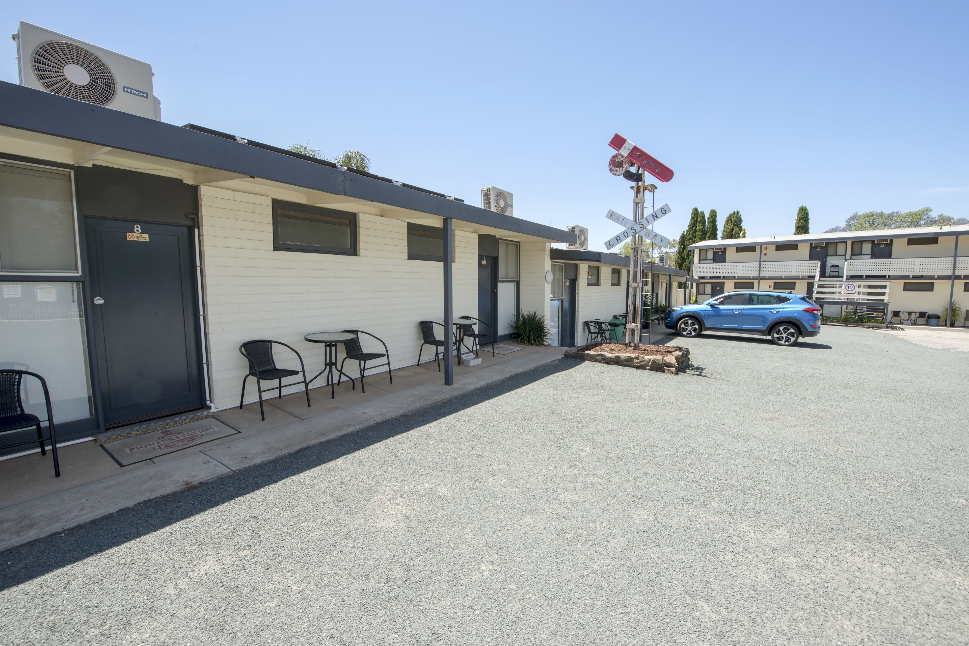 A motel with a single-story structure, a covered outdoor seating area, and a parking lot.