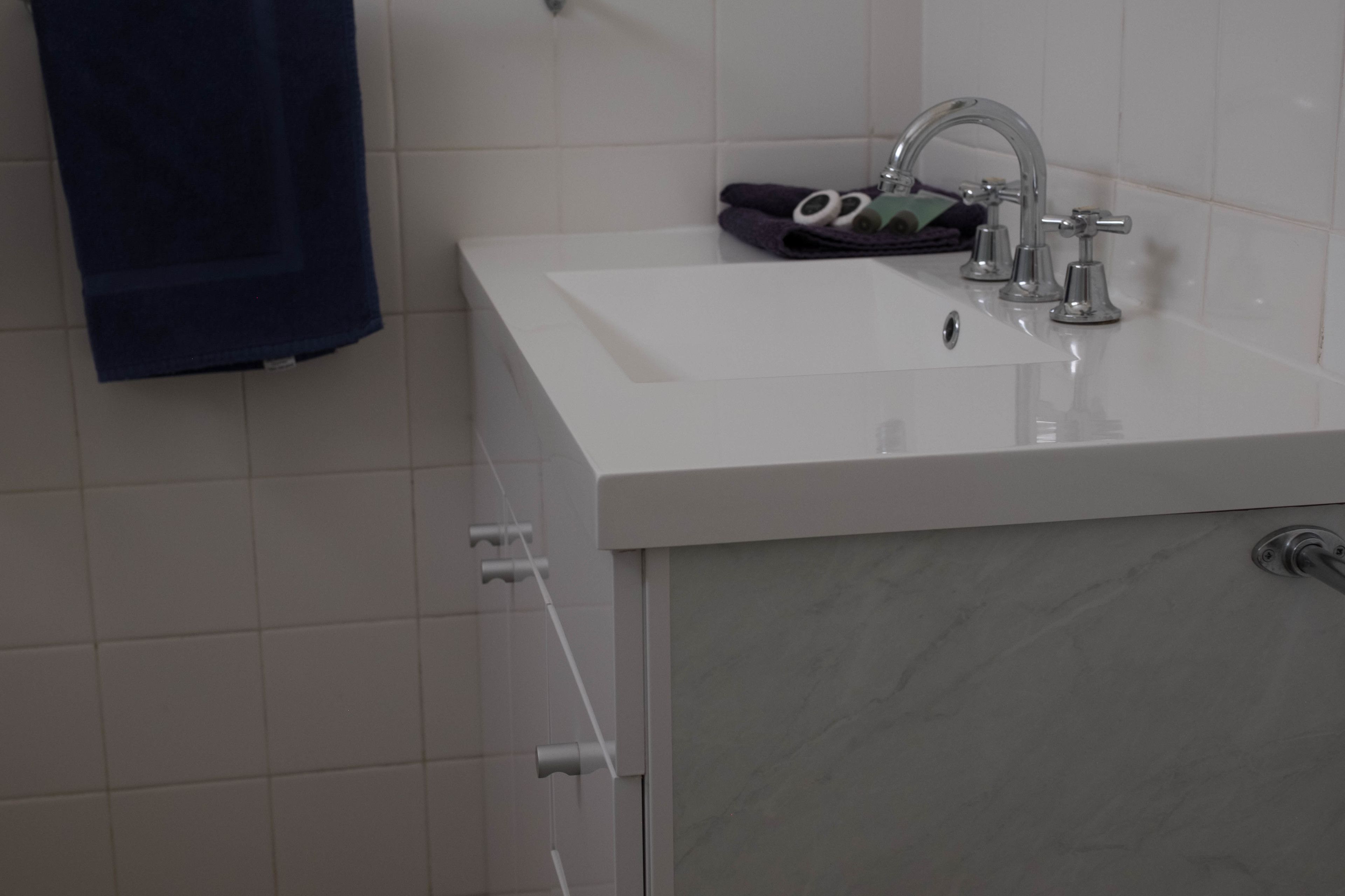 A bathroom with a white sink, a towel rack, and a marble countertop.