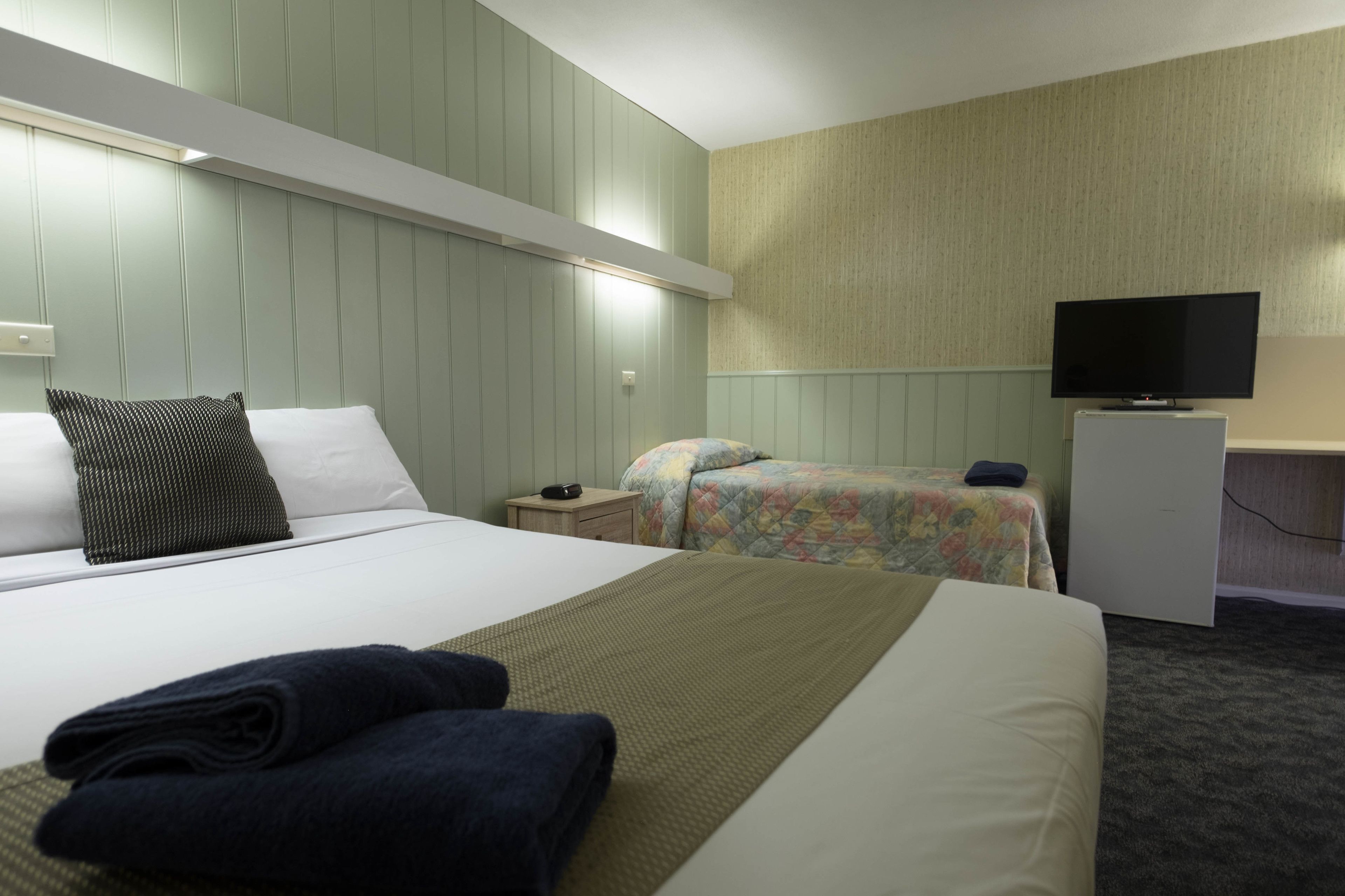 A hotel room with a large bed, a smaller bed, a desk with a television, and a carpeted floor.
