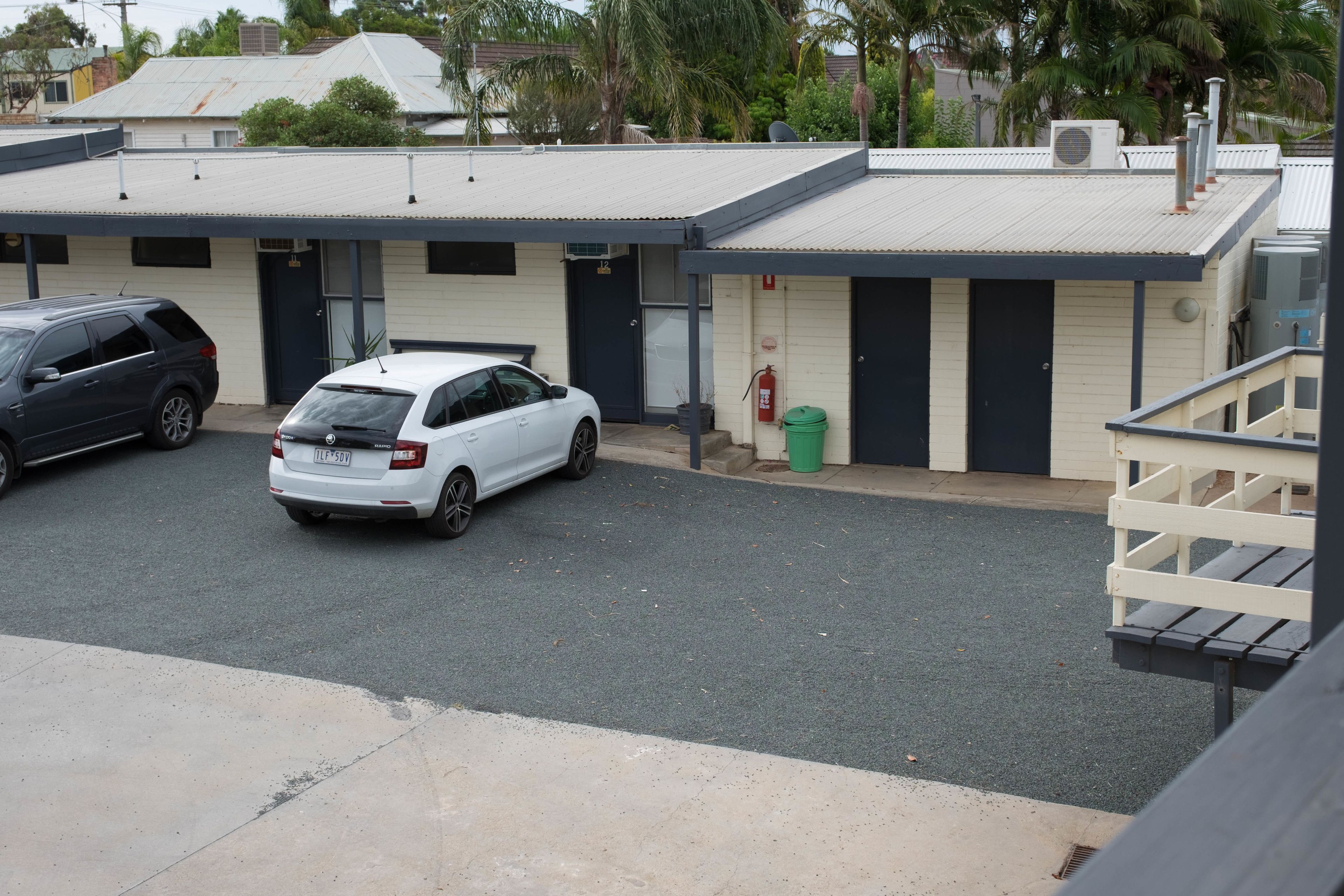 A building with a flat roof, a green trash bin, and a white car parked in front.