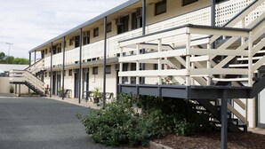 Un motel de varios pisos con una escalera central, mobiliario exterior y un área exterior cubierta.