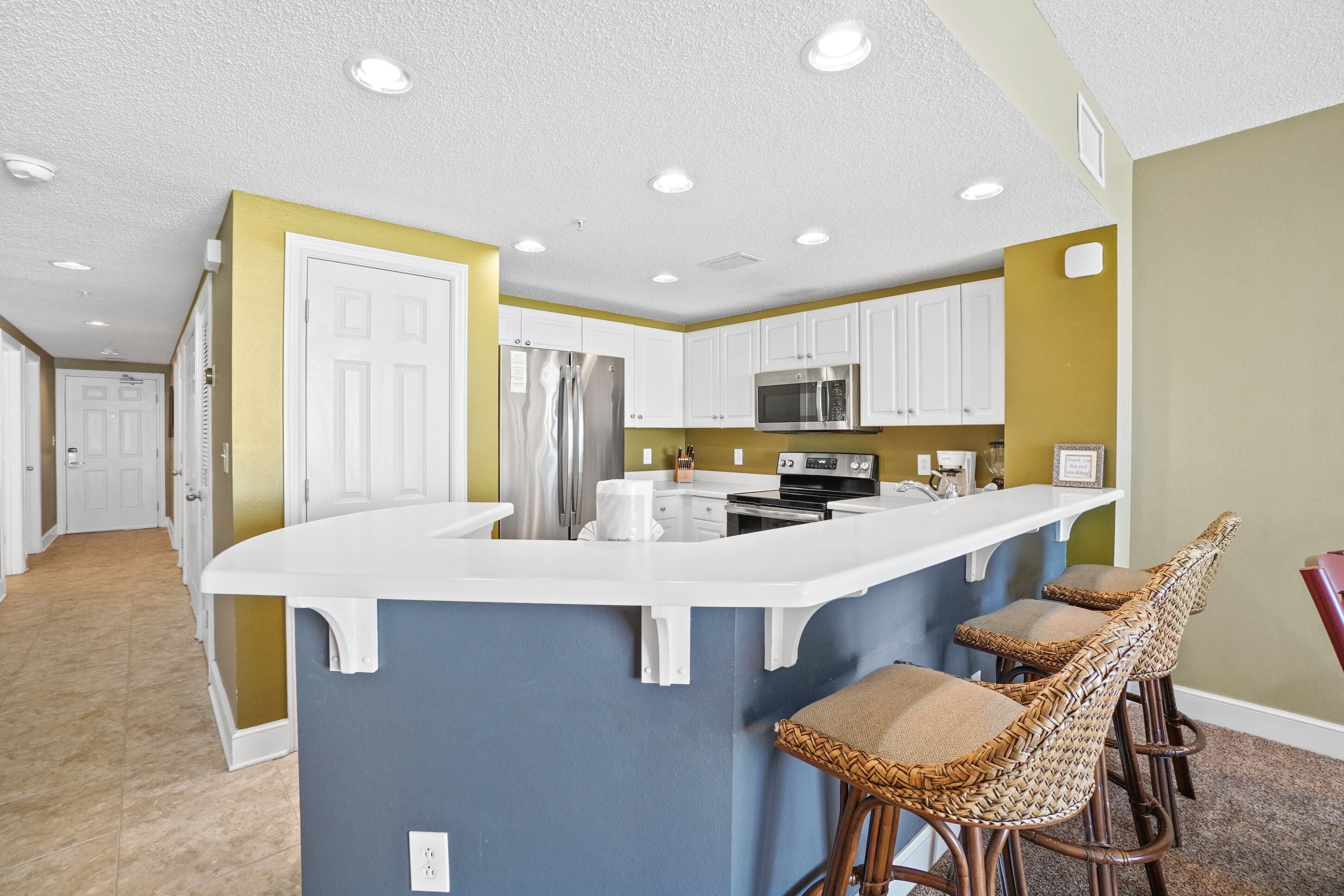 A kitchen with white cabinets, a stainless steel refrigerator, a microwave, and a white island with bar stools.