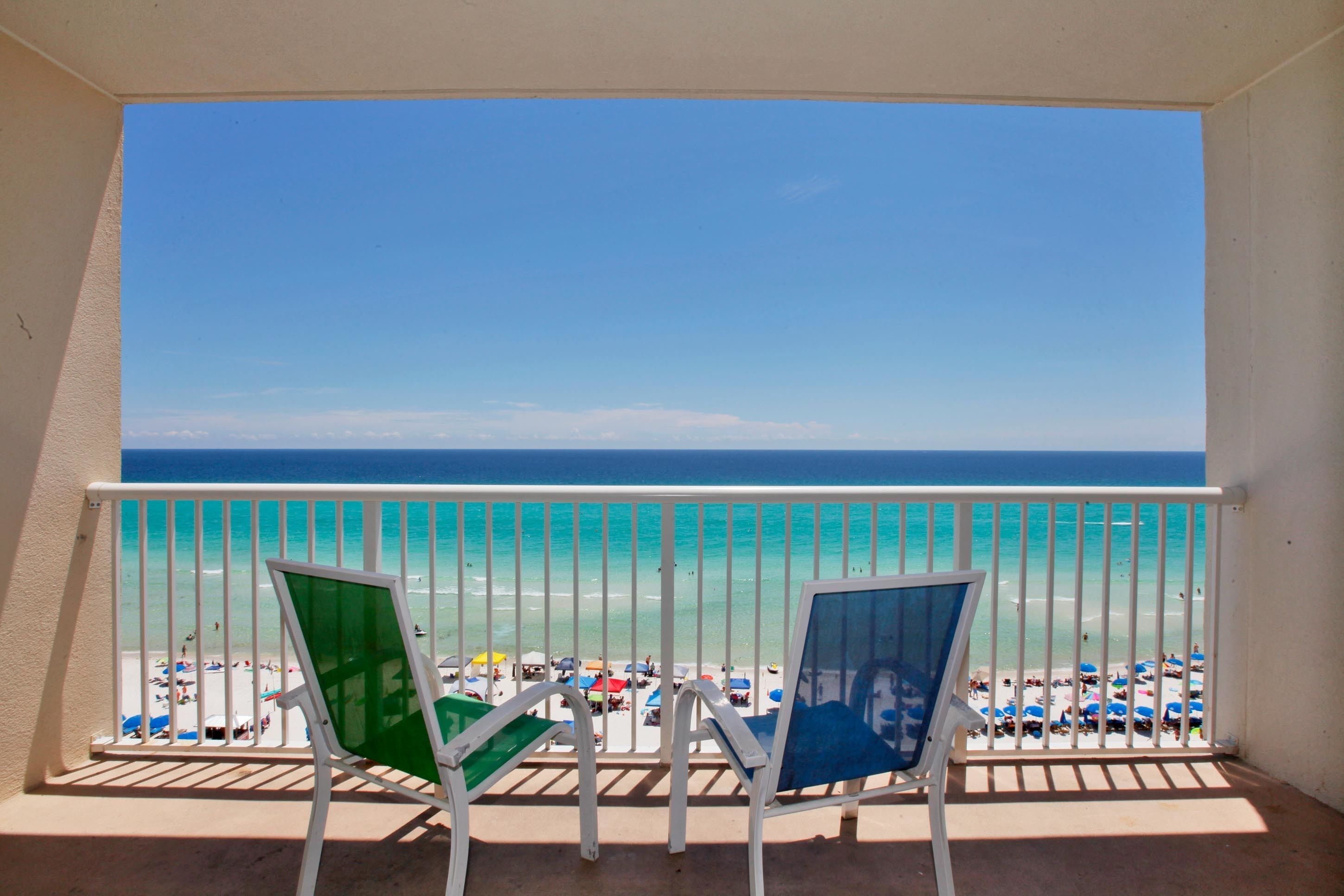 A balcony with two chairs overlooking a beach with clear turquoise water and a white railing.