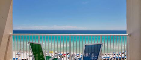 A balcony with two chairs overlooking a beach with clear turquoise water and a white railing.