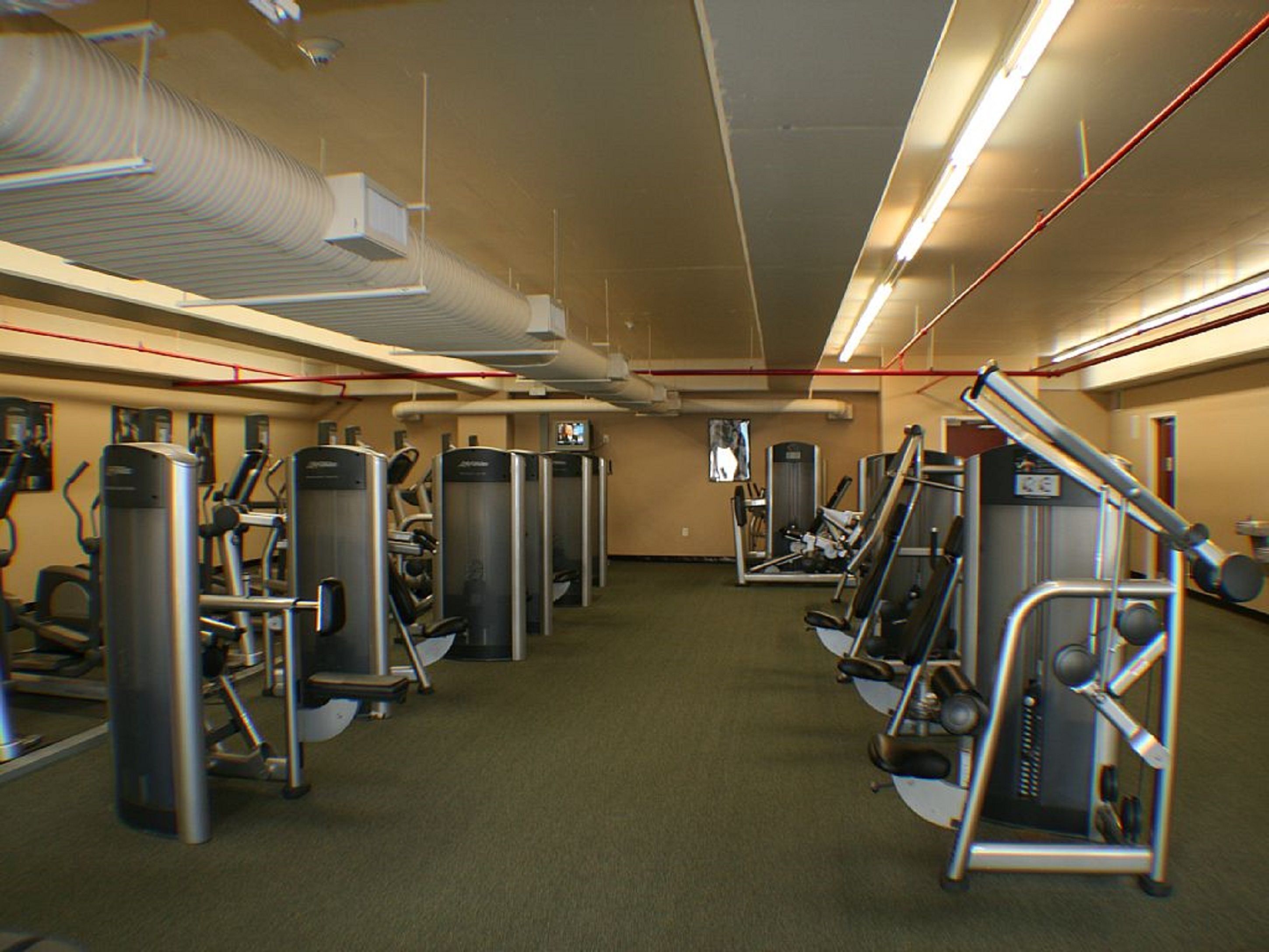 A gym with various exercise machines, a television screen, and a ventilation system.