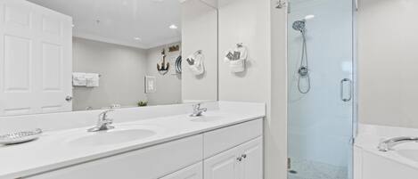 Un baño moderno con tocador doble, un espejo grande, ducha con mampara de vidrio y bañera separada.