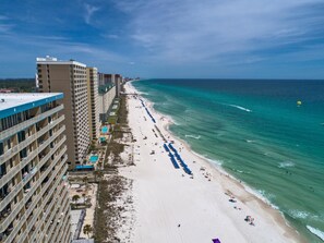 A beachfront hotel with multiple floors, a pool, and a beach with umbrellas.