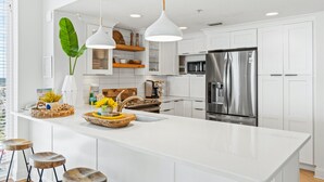 A modern kitchen with white cabinetry, stainless steel appliances, and a large island with stools. - Majestic Beach Resort by Panhandle Getaways (Panama City Beach)