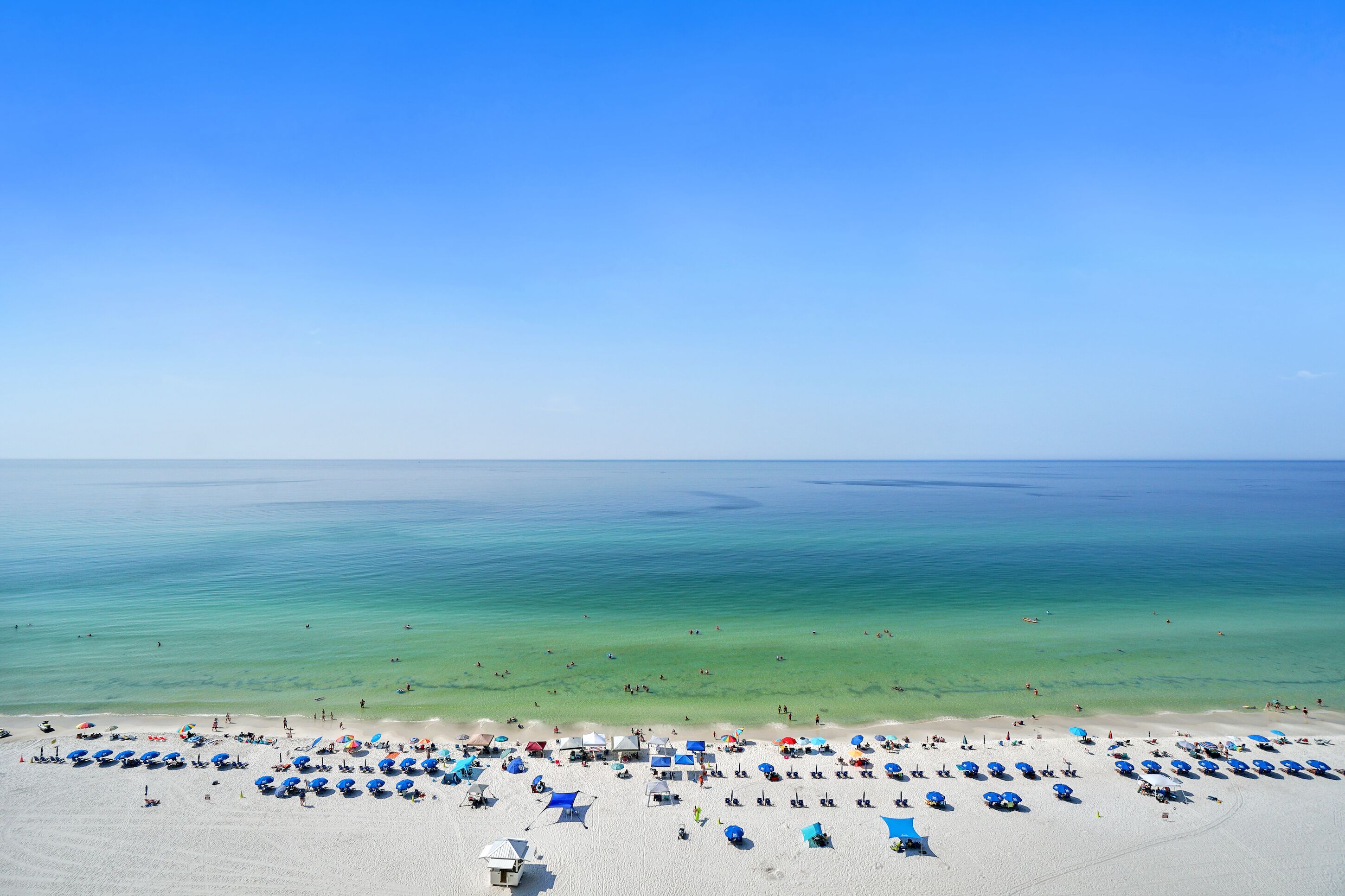 A beach with numerous umbrellas and sun loungers, a clear sky, and calm waters.