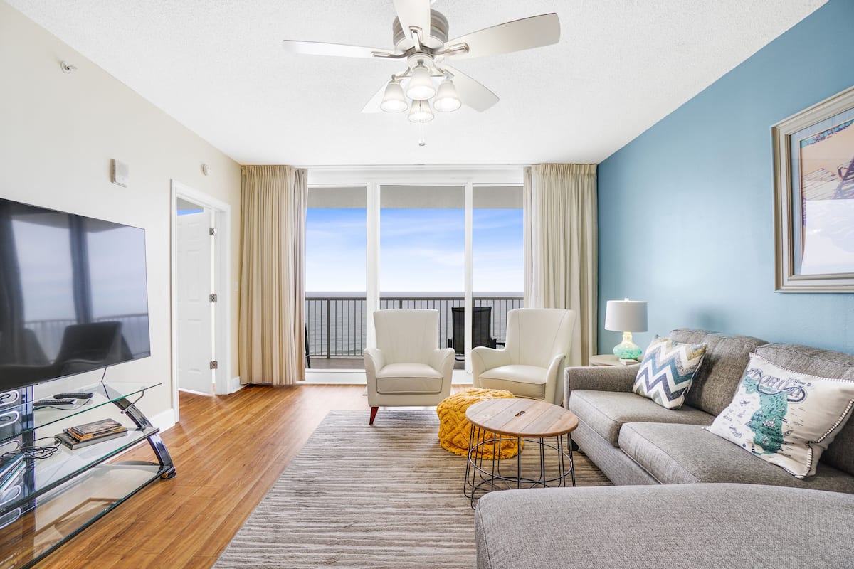 Un salon moderne doté d’un téléviseur à écran plat, d’un ventilateur de plafond, d’un canapé, de fauteuils et d’un balcon avec vue.