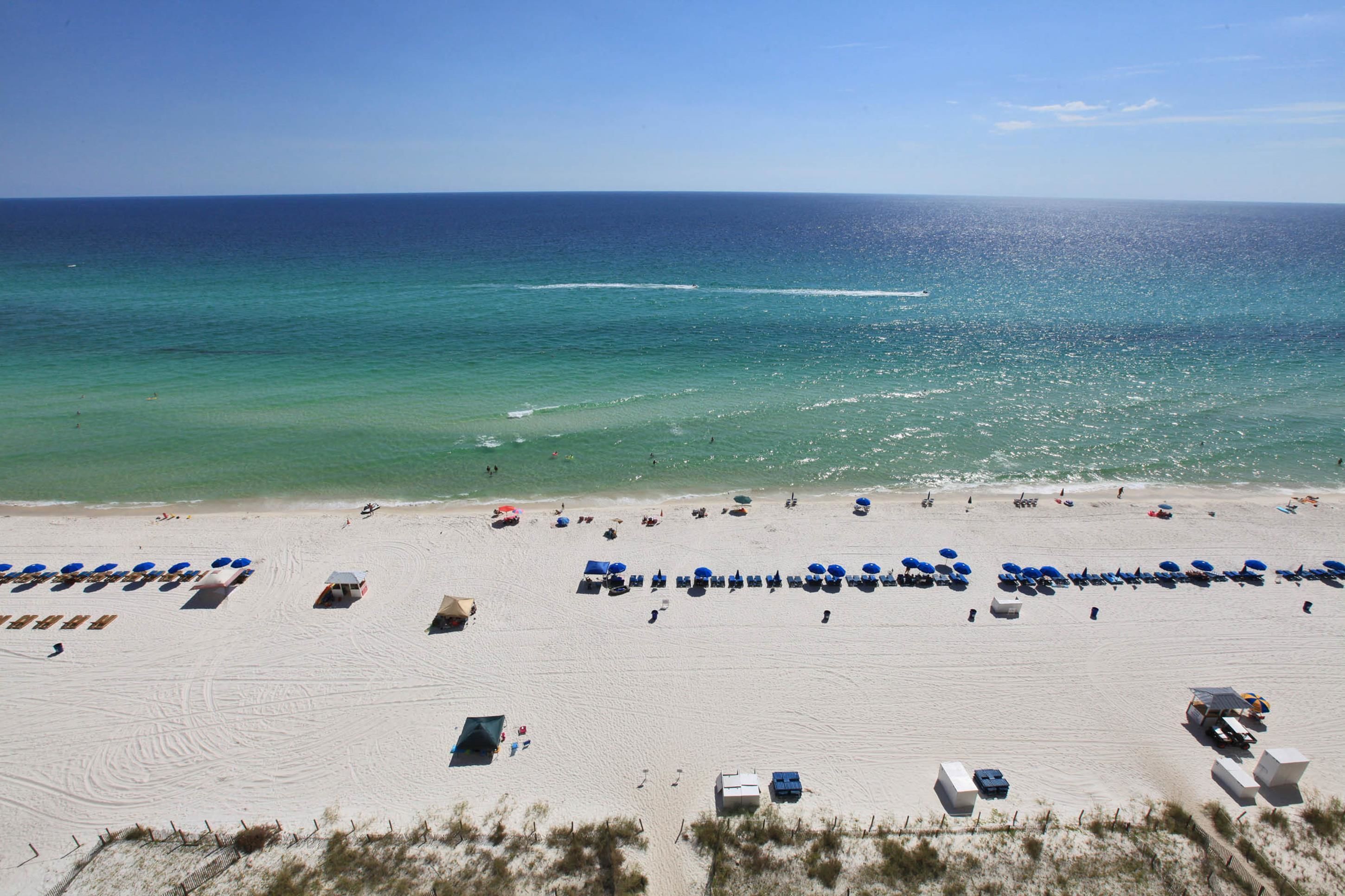 A beach with rows of sunbeds and umbrellas, a clear sky, and the ocean in the background.