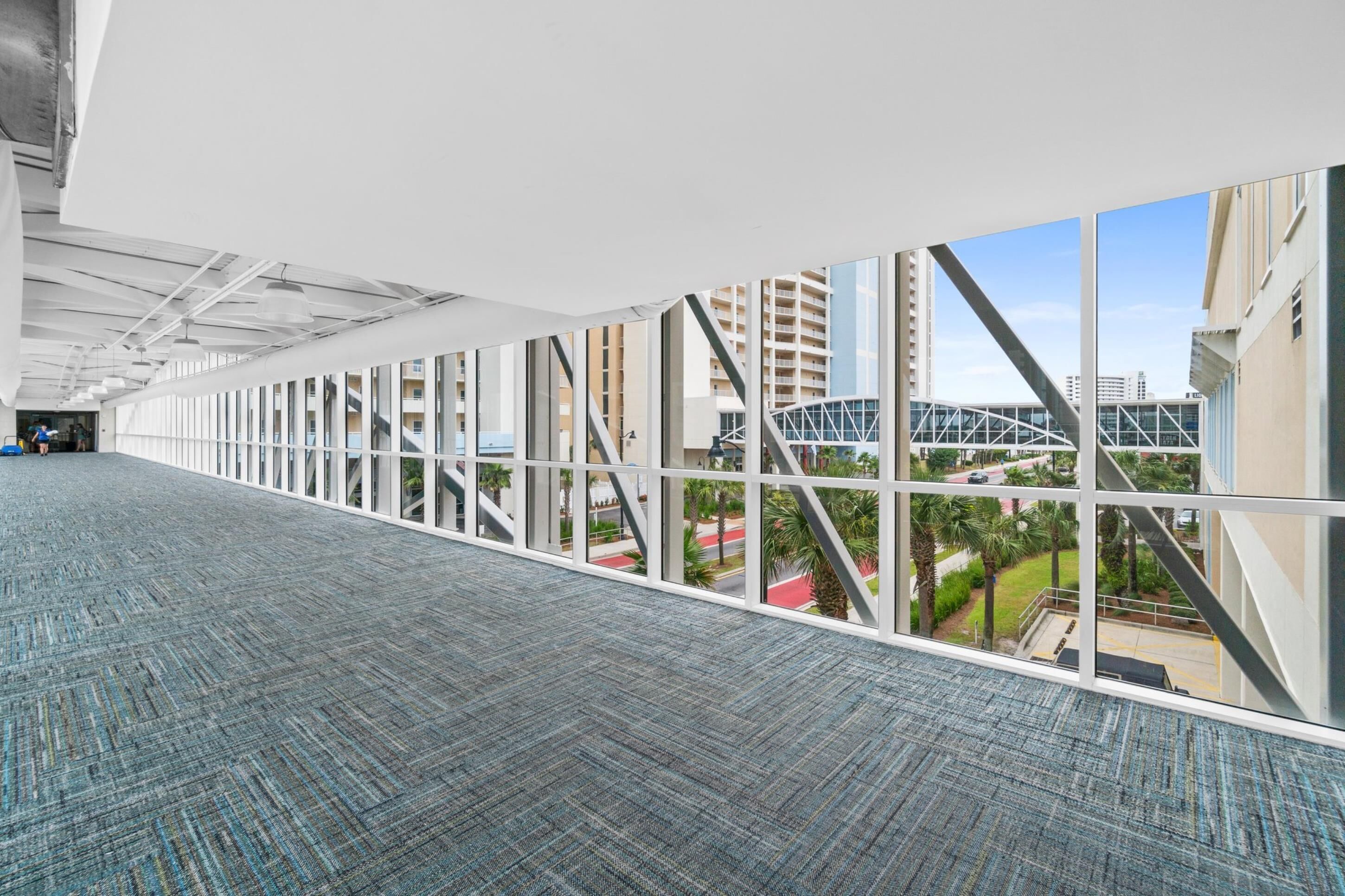 Un largo pasillo con ventanas amplias, alfombra estampada y vistas de edificios y un puente.