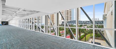 Un largo pasillo con ventanas amplias, alfombra estampada y vistas de edificios y un puente.