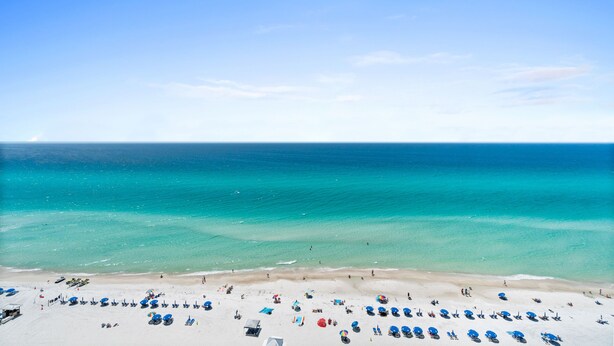 A beach with clear turquoise water, white sand, and numerous blue umbrellas. - Majestic Beach Resort by Panhandle Getaways (Panama City Beach)