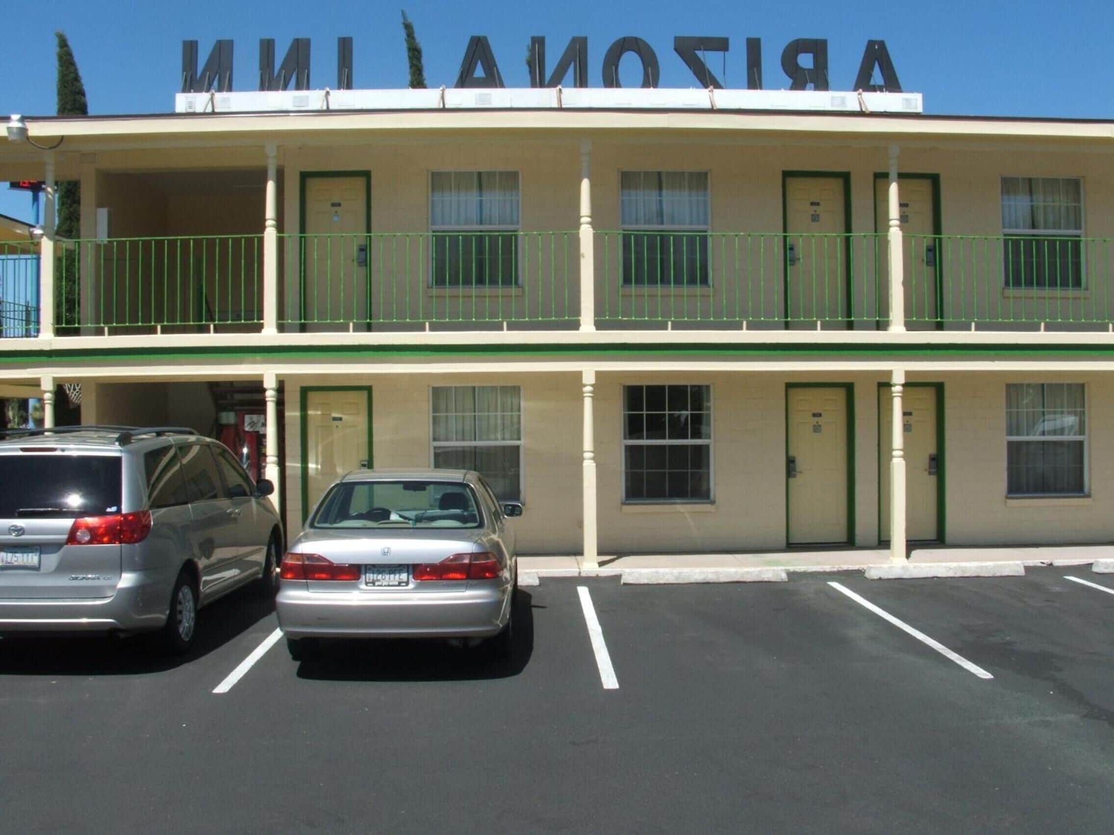 A two-story motel with a green and white facade, multiple balconies, and a parking lot with two cars.