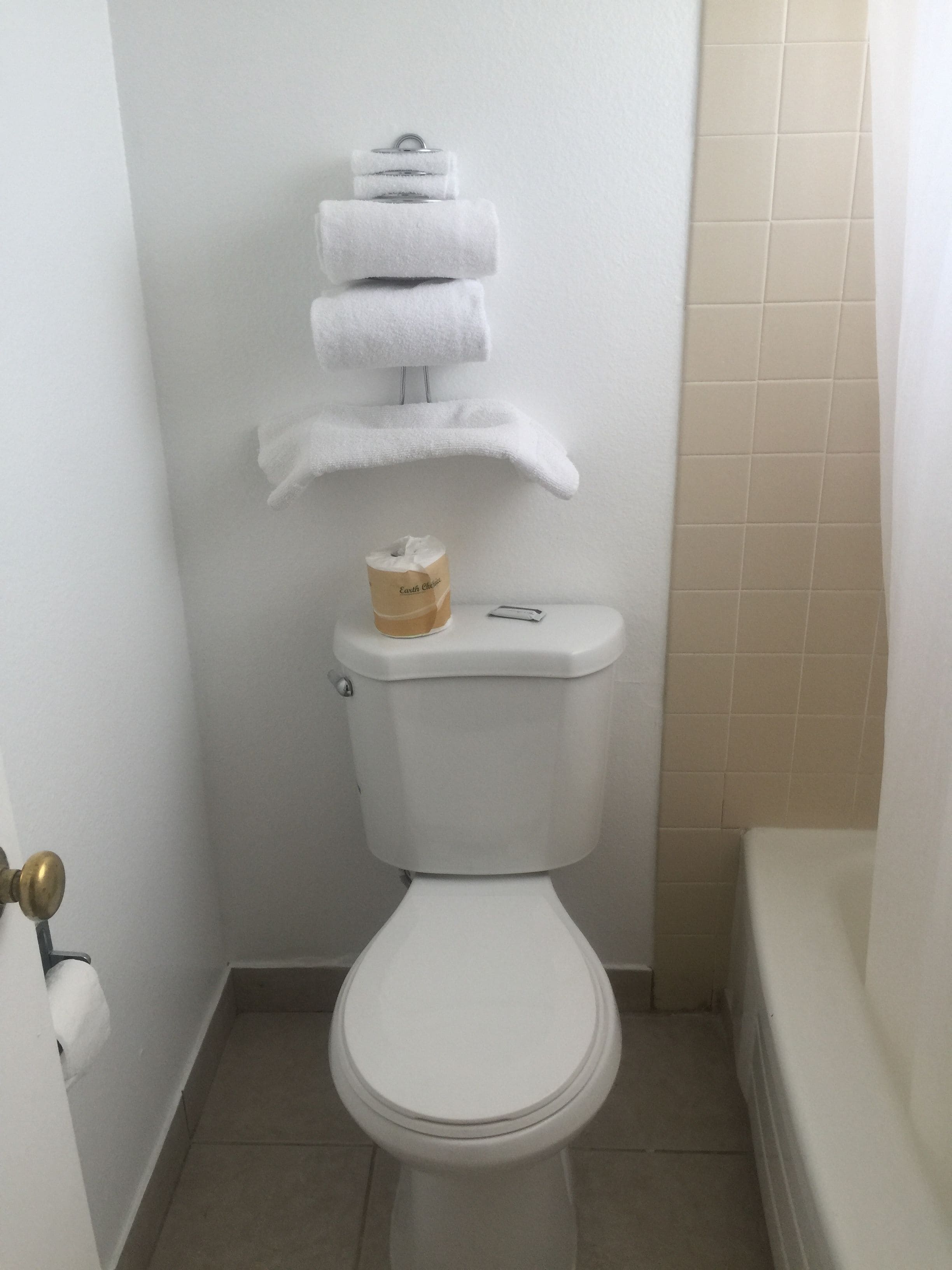 Een toilet met een stapel witte handdoeken op de tank, een toiletrolhouder en een toiletrol.