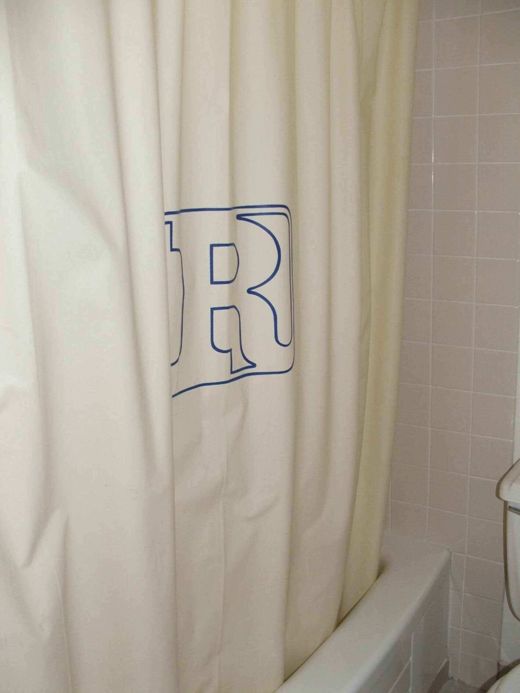 A bathroom with a white bathtub and a shower curtain featuring a large 'R' logo.