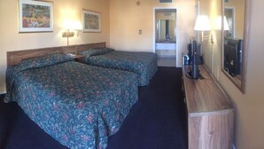Une chambre d’hôtel avec deux lits, une petite table, une chaise, un bureau, un miroir et un téléviseur.