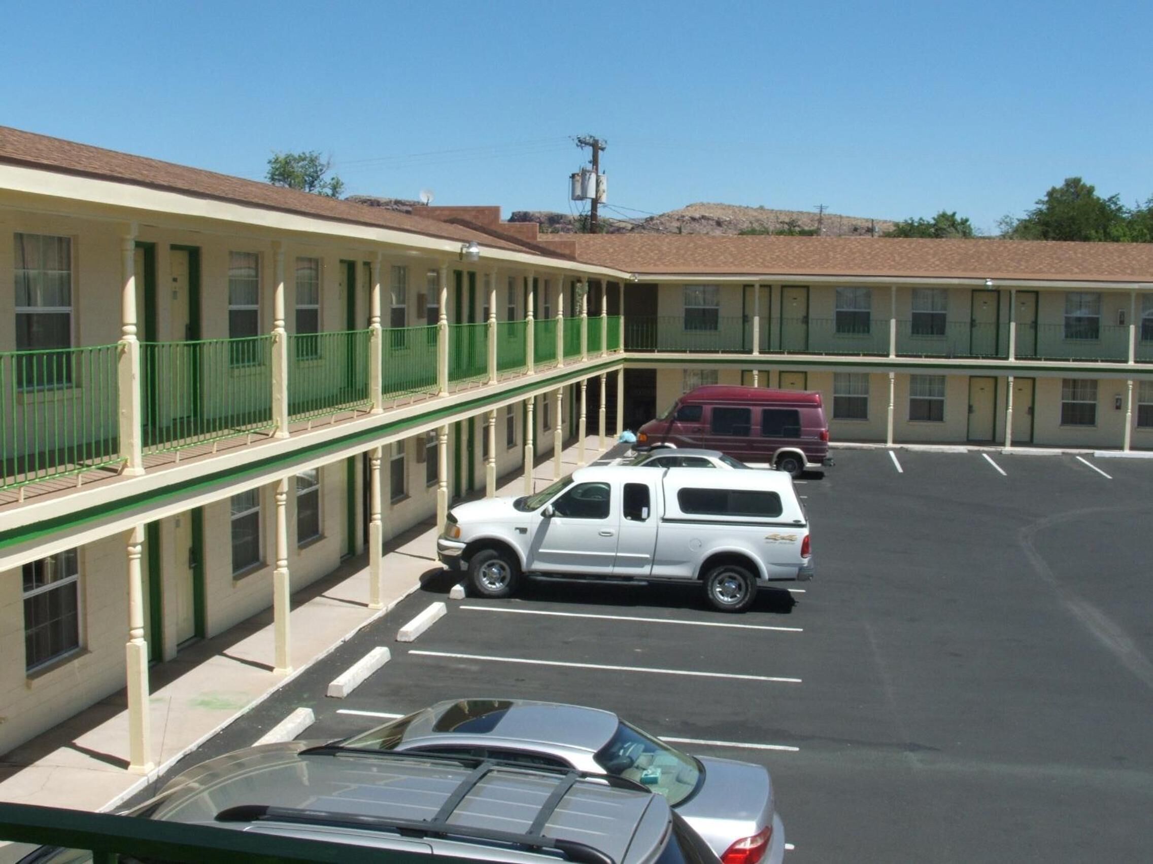 Egy motel, amelyhez tartozik egy parkoló, egy fehér, platós teherautó, és egy piros színű furgon, melyek a parkolóban állnak.
