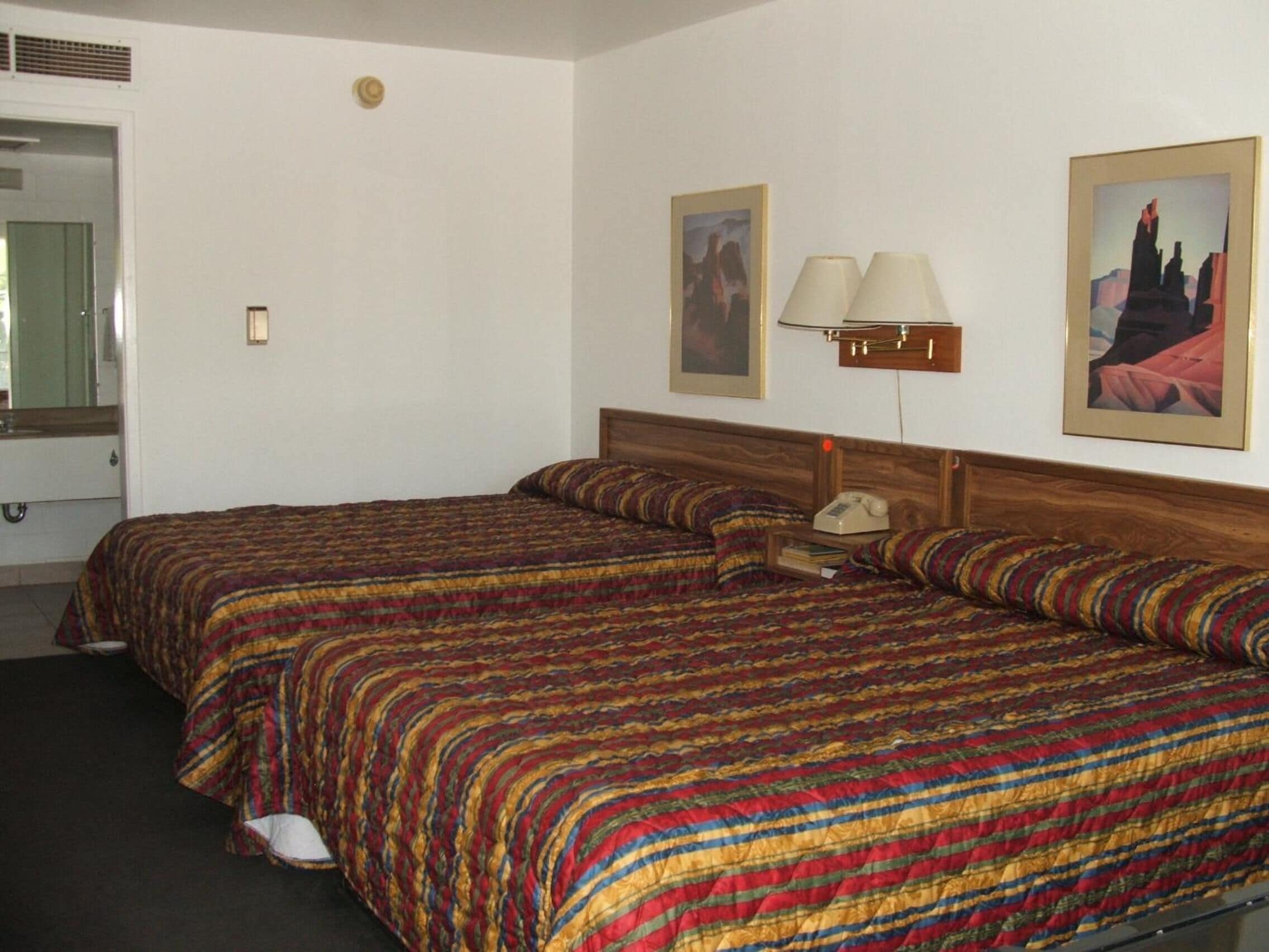 A hotel room with two beds, a mirror, a lamp, and two framed pictures on the wall.