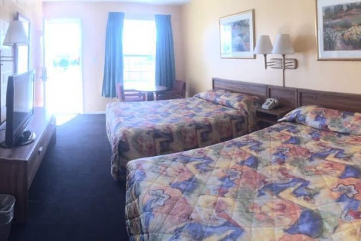 A hotel room with two beds, a desk, a chair, a TV, and a window with curtains.