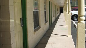 Une rangée de chambres de motel avec des portes et des fenêtres vertes, une allée couverte et une voiture garée à l’arrière-plan.