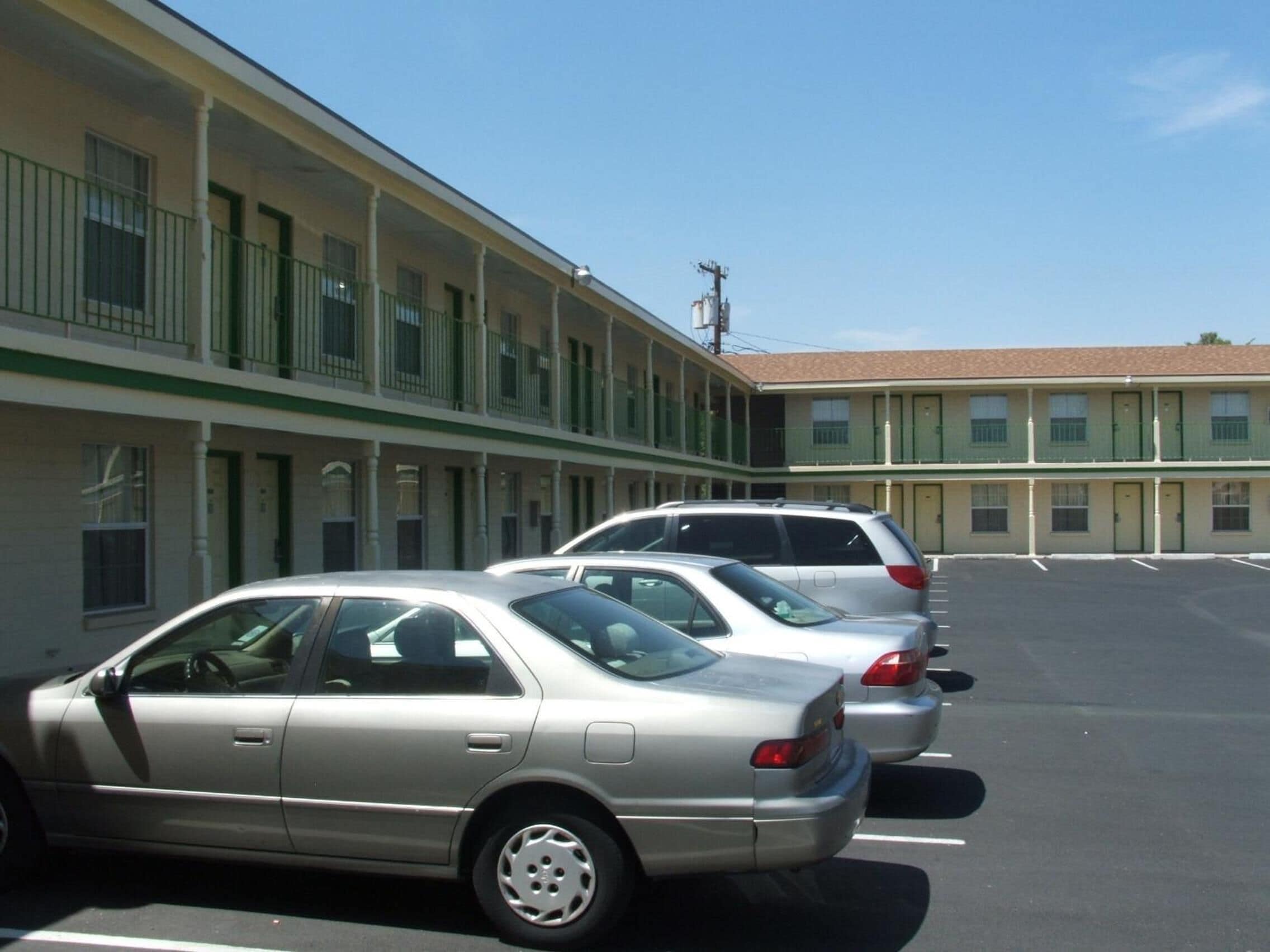 A motel with a row of rooms, each with a balcony. There are three cars parked in the parking lot.