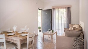 A dining area with a wooden table set for four, white chairs, and a small side table with a vase.