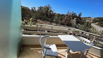 A balcony with a table and chairs, overlooking a hilly landscape with trees and a road.