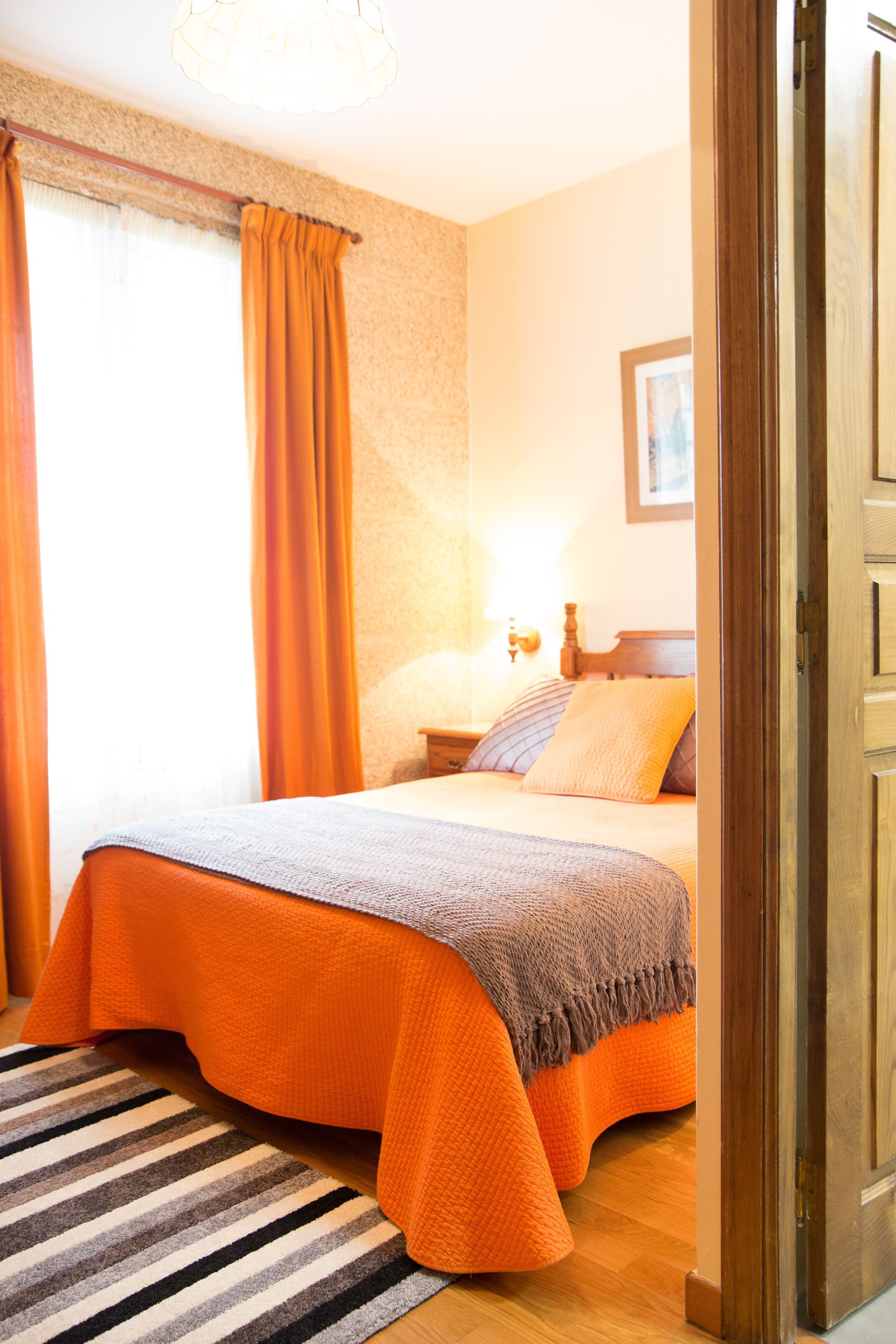 A hotel room with a bed, a nightstand, a lamp, and a window with curtains.