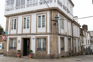 A corner building with a white facade and multiple windows. There are potted plants at the entrance. - Linares Rooms Santiago (Santiago de Compostela)